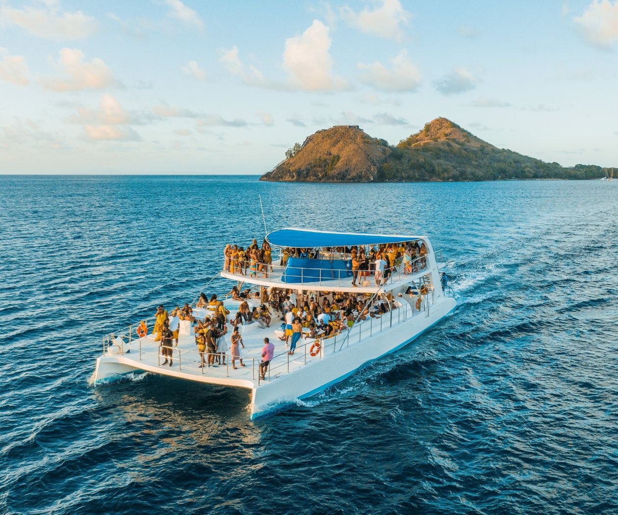 Luxury catamaran yacht with enthusiastic tourists enjoying a lively party atmosphere onboard.