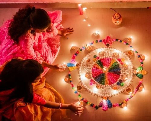 Two Indian Wowen Lighting Diyas and decorating Rangoli with flowers on the occasion of Diwali Festival, The Festival of Lights