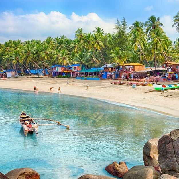 A panoramic view of a beautiful sandy beach in Goa, India with crystal-clear blue water, coconut trees, and clear blue sky