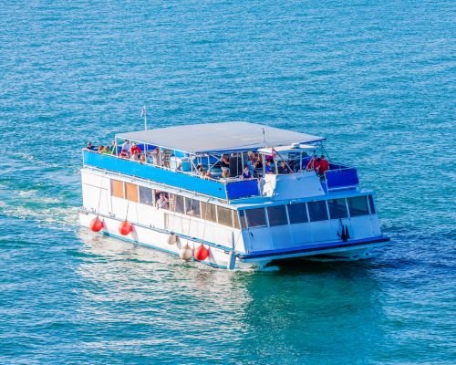 Catamaran yacht with enthusiastic tourists on open deck, sailing on calm blue sea.