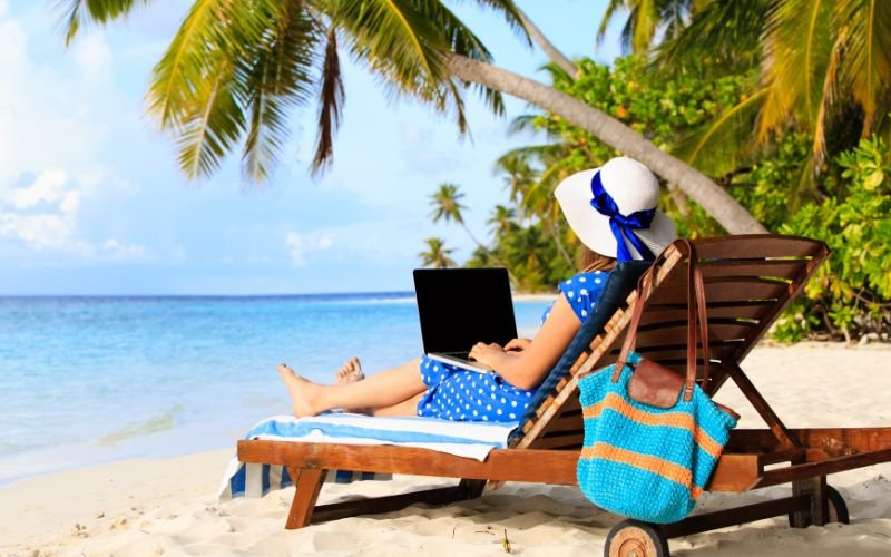 Woman on vacation sitting on beach chair with laptop.