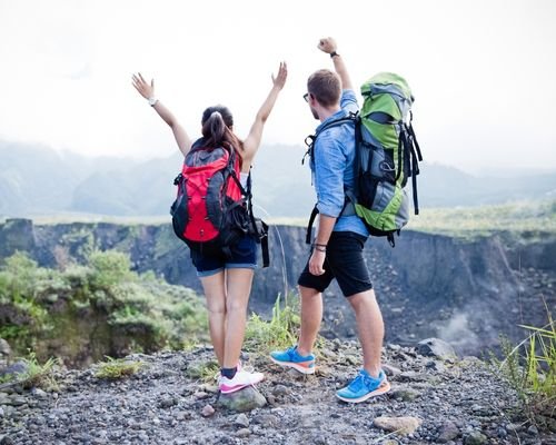 A couple of people trekking through lush green forests and rocky terrain in Goa, India.